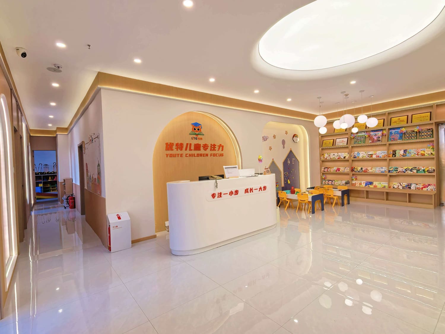 校区阅读与陈列区：整面低矮书架摆满儿童读物与教具盒，上方陈列资质牌匾